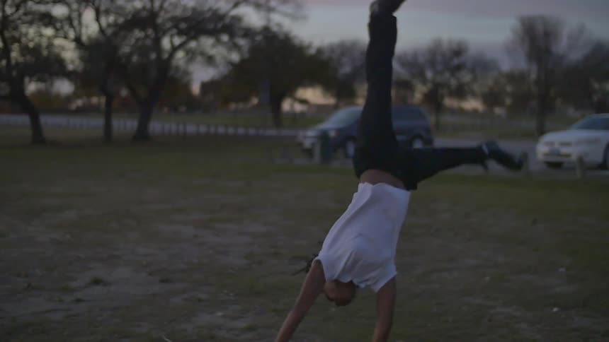 A girl does a handspring in a field at sunset