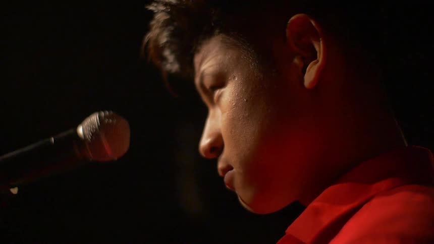 A man standing at a microphone with  lights shining down on him