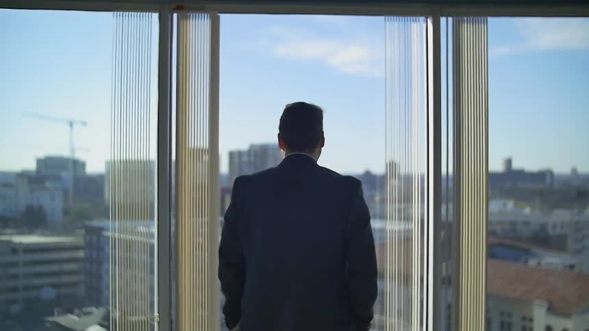An man in a suit looks out a window in the city