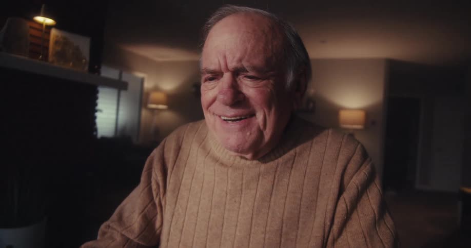 Elderly man laughs while watching his computer screen at home at night
