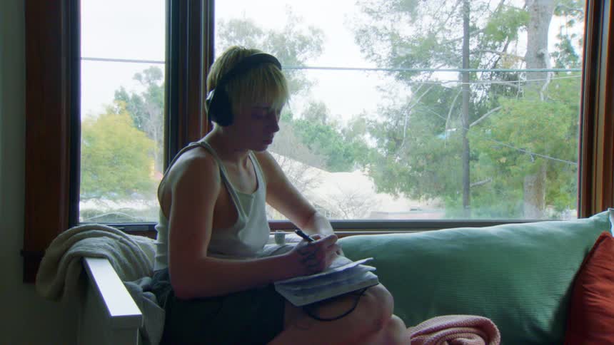 A woman writes in her notebook while sitting by the window