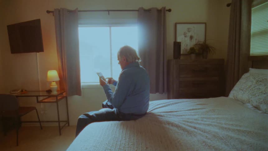 Elderly man sitting on bed using cell phone
