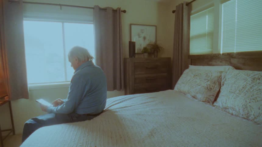 Elderly man sitting on bed using tablet
