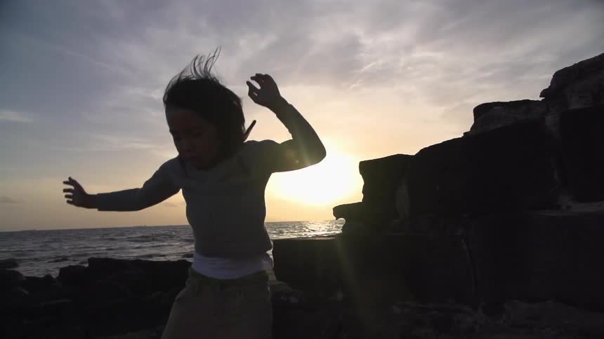 Child jumps off rocks as the sun sets