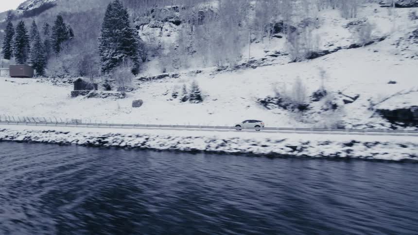 A car drives on the road by the shore covered in snow