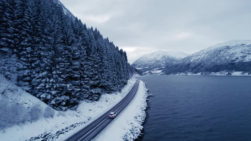 Car traveling along a road along a lake in an environment surrounded by snow and coniferous forest