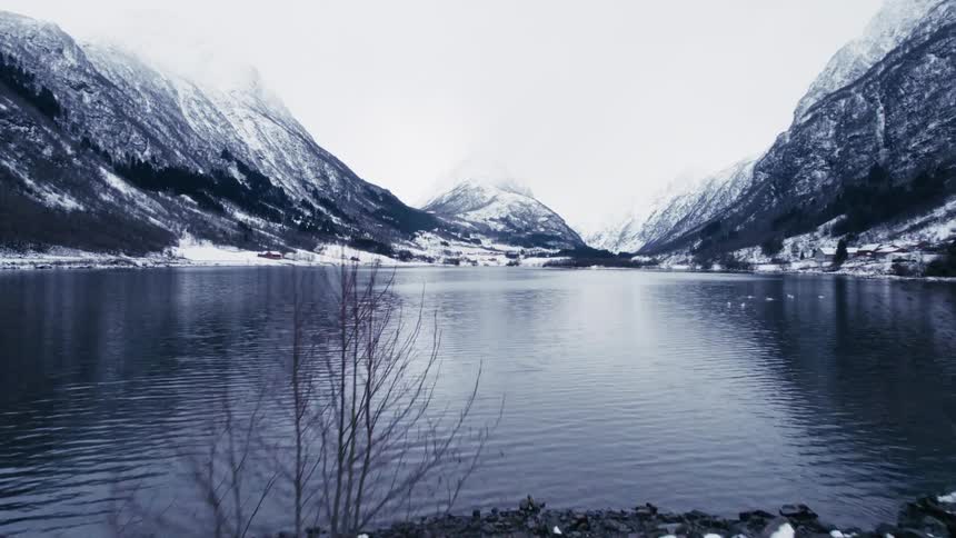 A white car stopped on a road next to a huge lake between a range of snowcapped mountains