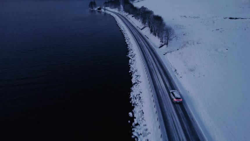 Aerial view of cars driving on a freeway by the sea and a mountain range during winter