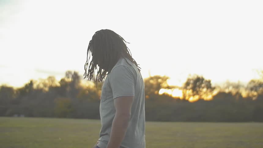 A man is walking across the grass field at sunset