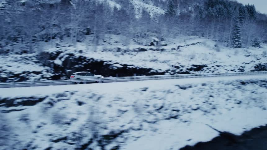 A car driving on a road that is covered in snow next to a lake