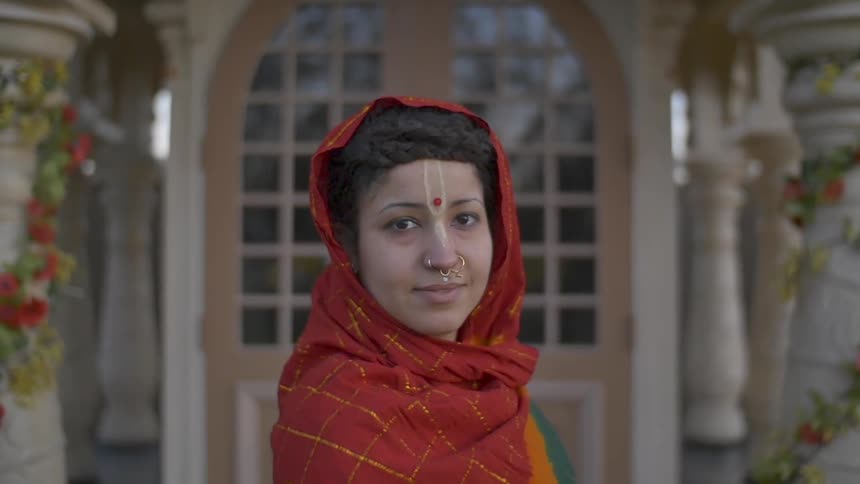 Indian woman in traditional garb stands outside a house