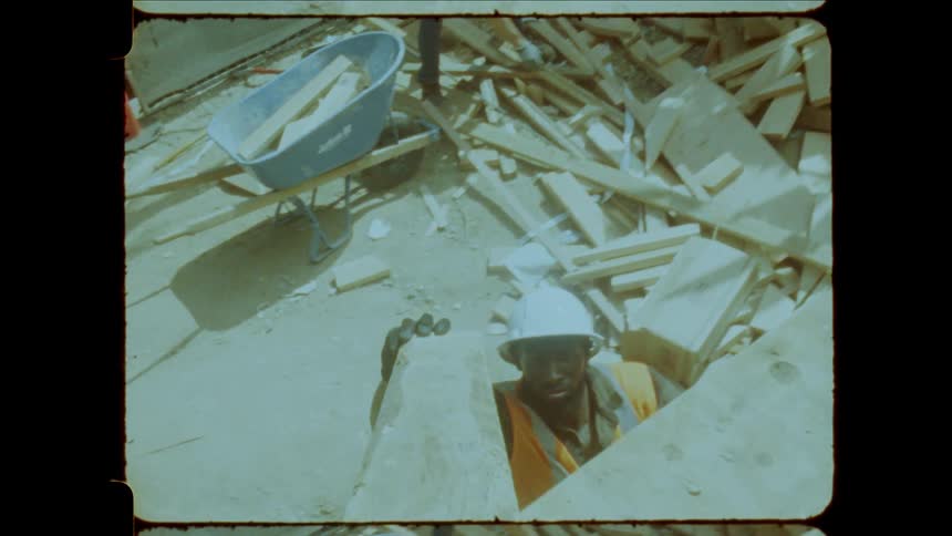 Construction workers in hard hats lift and move wood amidst debris at a busy worksite