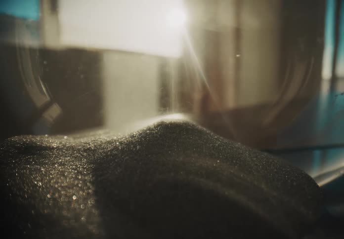 Black sand flows through an hourglass in warm glowing sunlight