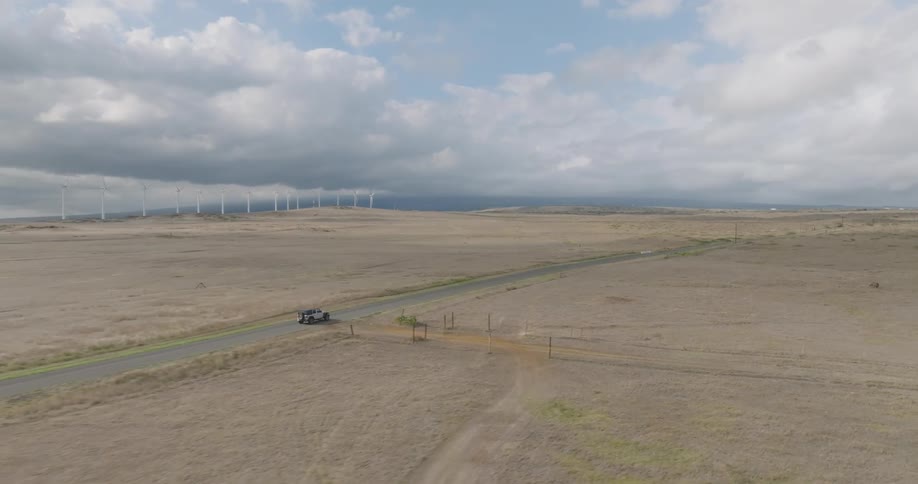 A car drives by the windmills on the field