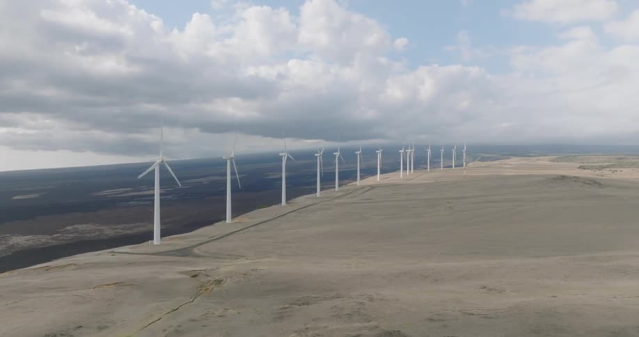 Long row of wind turbines stretches across a barren plateau under a partly cloudy sky