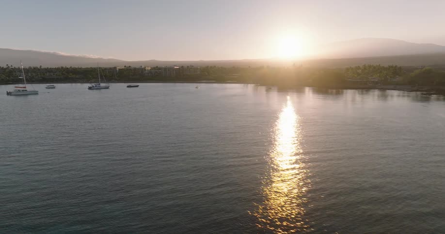 Aerial view of sailboats near a tropical coast at sunset golden light on calm water