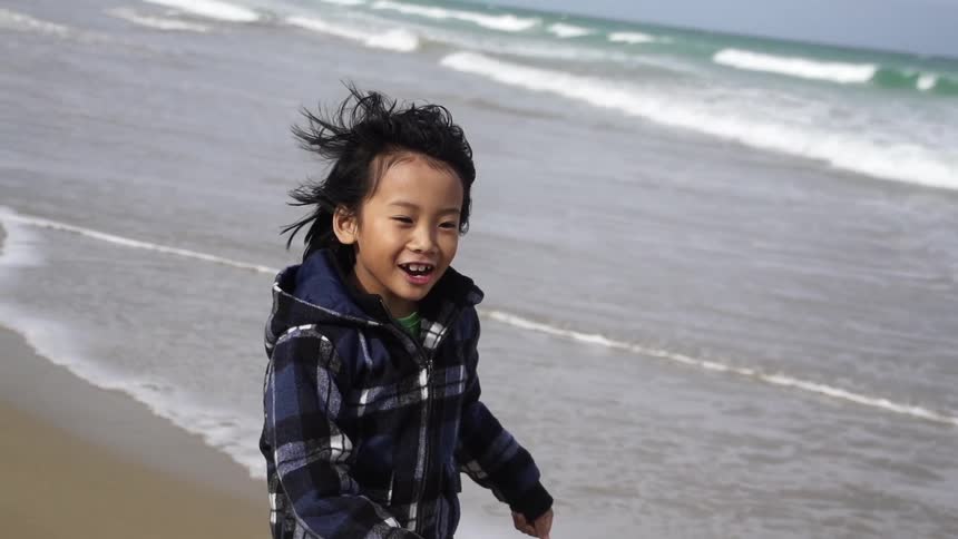 A smiling child runs beside waves on a beach