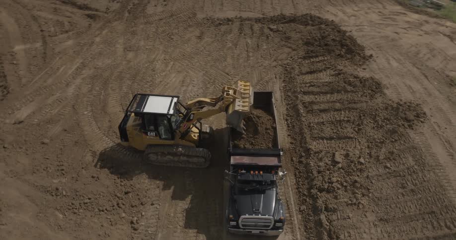 An excavator loads sand into the back of a truck on a sunny day