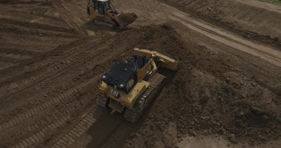 Multiple bulldozers move dirt while a dump truck exits the site onto a road