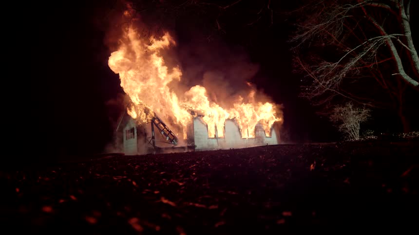 Intense flames burning a house in a rural area in slow motion at night