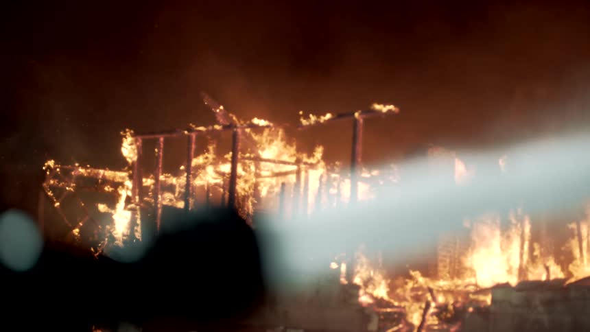 Fire hose close up forcefully spraying water on flames in the distance