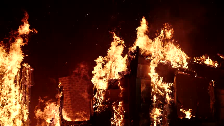 Flames engulf a structure with a brick chimney visible amidst the intense fire