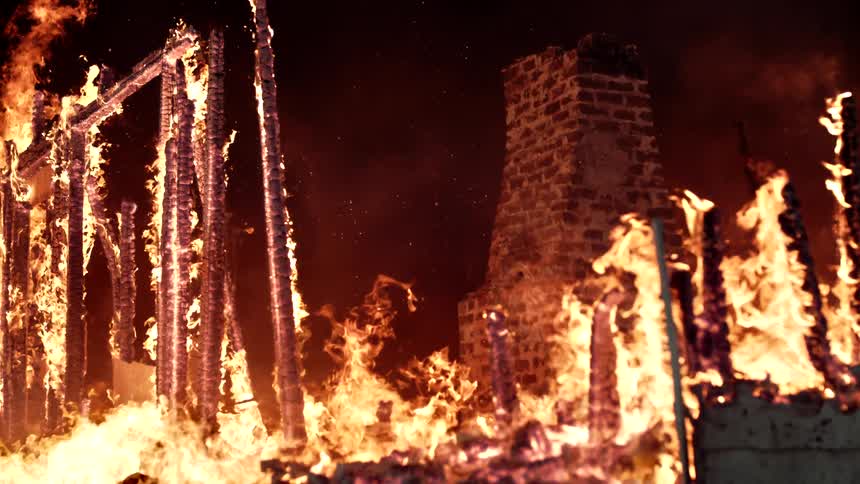 Brick fireplace stands amidst a mostly destroyed burning building at night