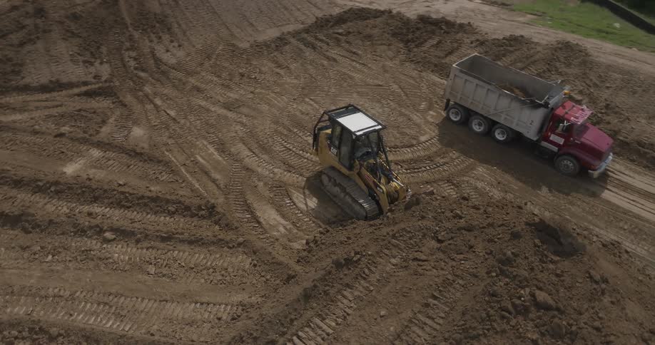 An excavator packs sand and loads it into a truck while another excavator gathers the sand into one section