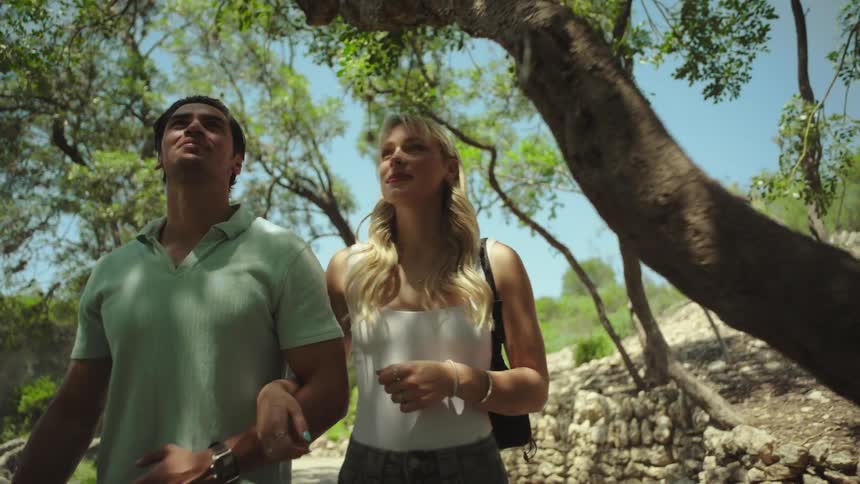 Couple walks arm in arm along a path through a park on a summer day