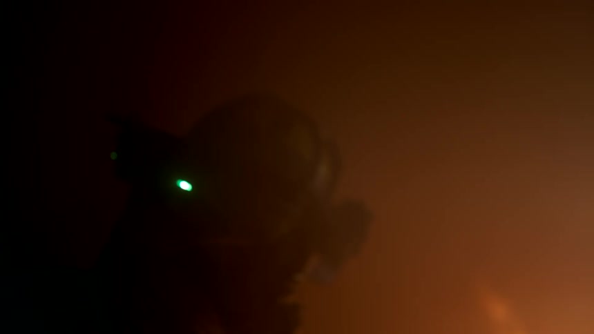 A firefighter wearing a mask holds a hose at night directing it toward the burning fire