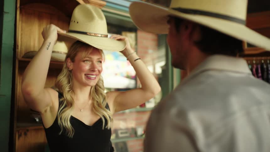 A man and woman try on cowboy hats in the store