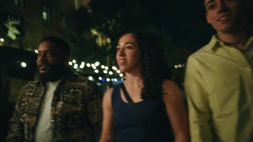 Two men and a woman talking and laughing while walking in a city at night