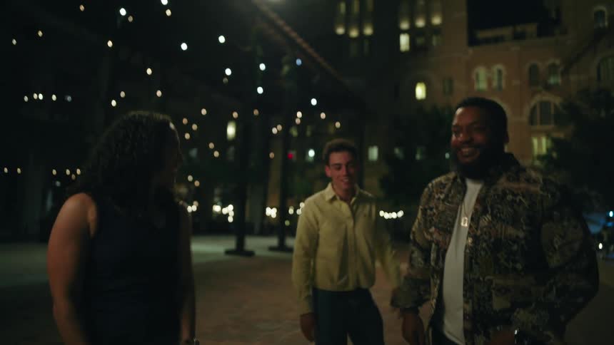 Two men and a woman walking talking and laughing on a city street at night