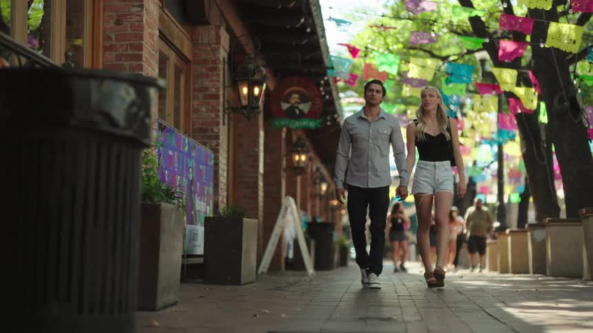 A couple hold hands while walking past the shops