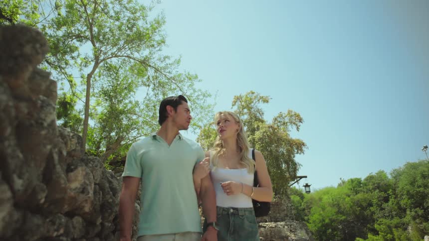 A man and a woman with used hands are walking in an outdoor environment near the stone wall and with trees in the background