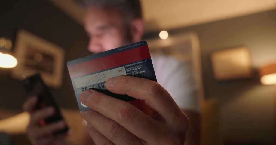 A man types on his cellphone as he looks back and forth from his credit card