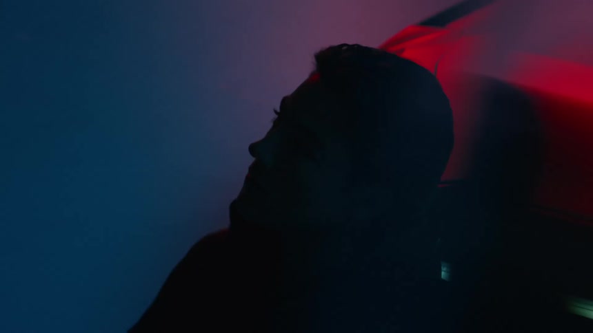 A close up of a man reclining on a modern sports car illuminated by flashing blue and red lights