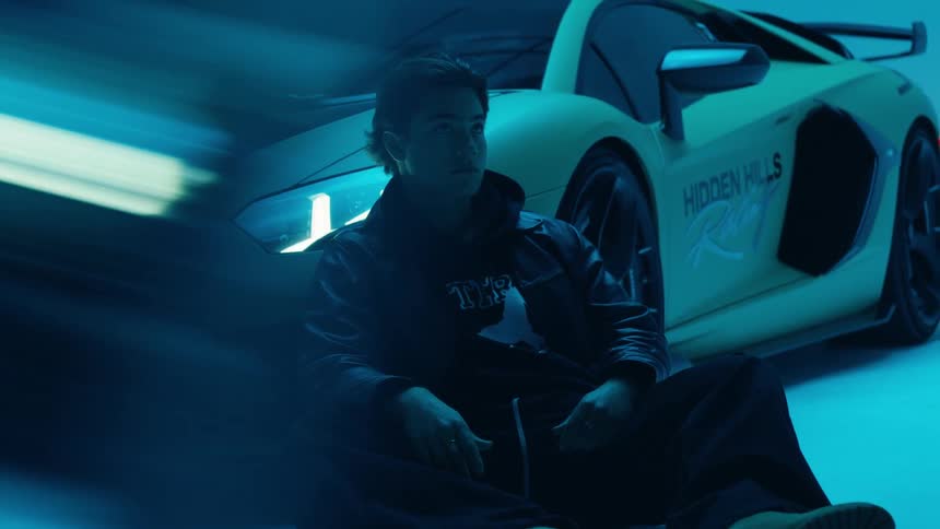Man sitting on the ground leaning against a sports car during a photo shoot