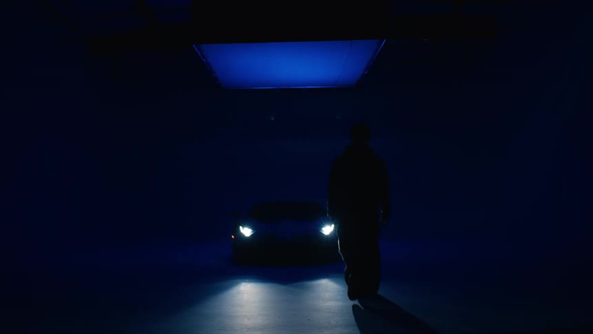 Man silhouetted by the light walks toward a newly parked car under a large light
