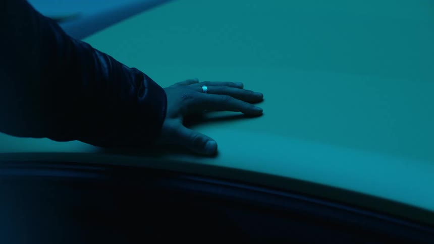 A hand rests on the roof of a car illuminated by flashing blue and red lights