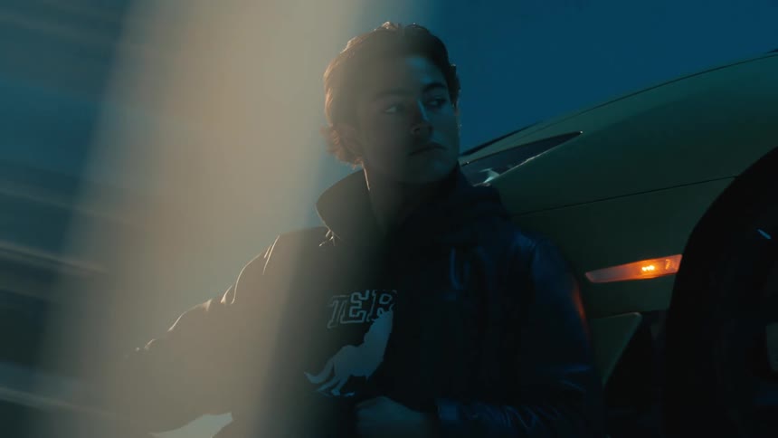 Man leans against a sports car in an area lit by a flashing blue light