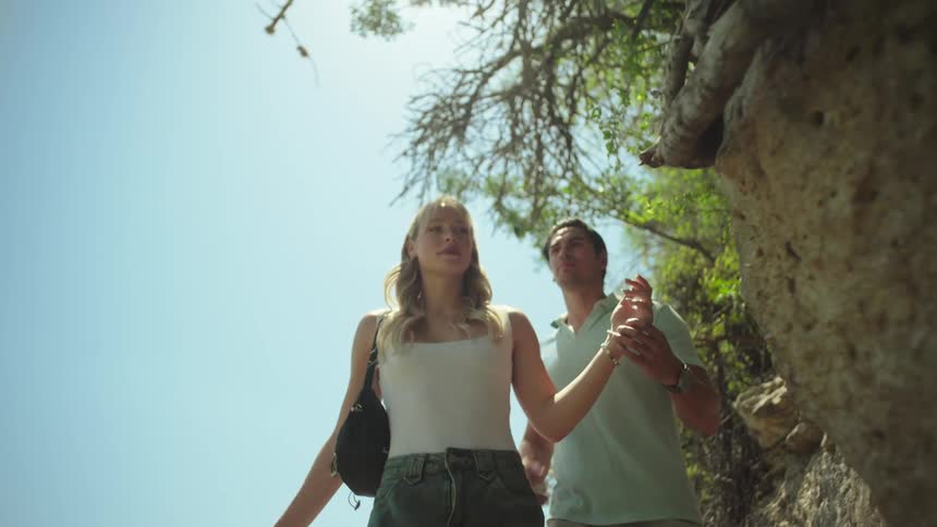 A man and woman are hiking past a large boulder