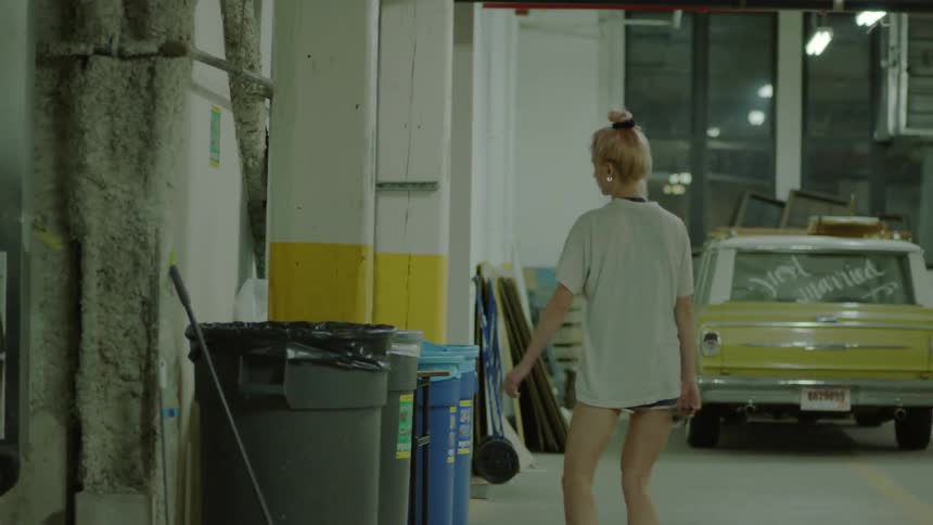 A woman walks through a lot and throws away garbage