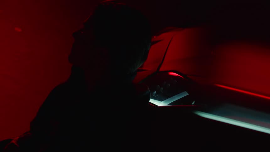 A young man sitting on the ground leaning against a sports car under red lights