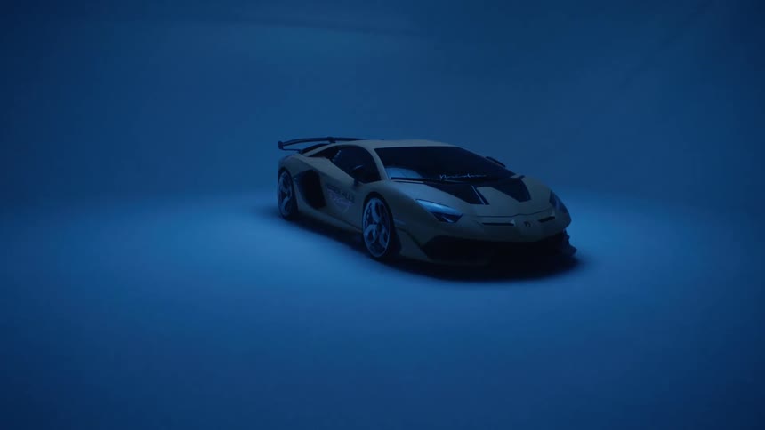 A yellow lamborghini sports car is revealed under blue studio lighting