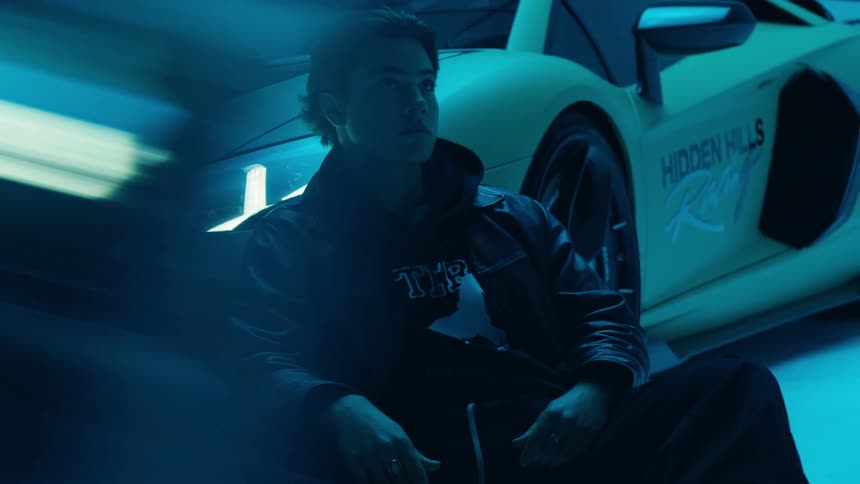 A female driver leaning against a sports car while neon lights are blinking above her