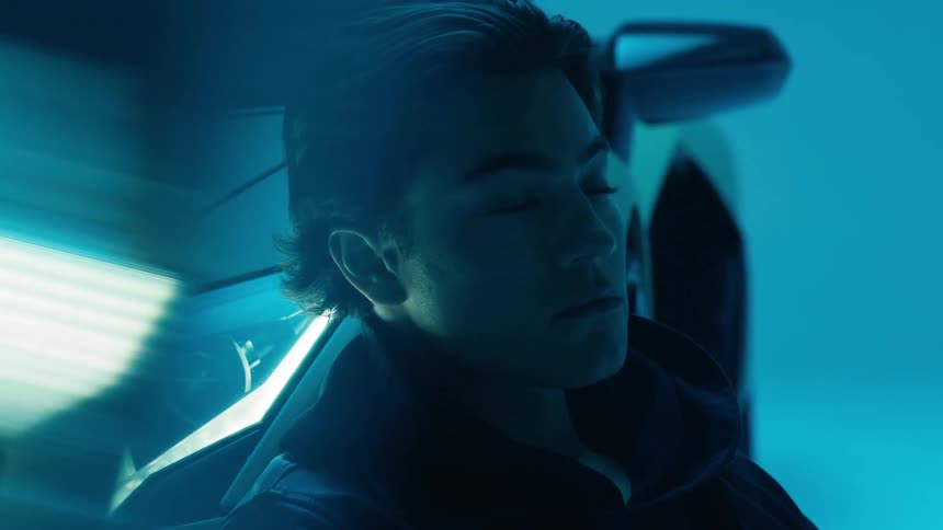 A young man sitting and leaning against a sports car during a photo shoot