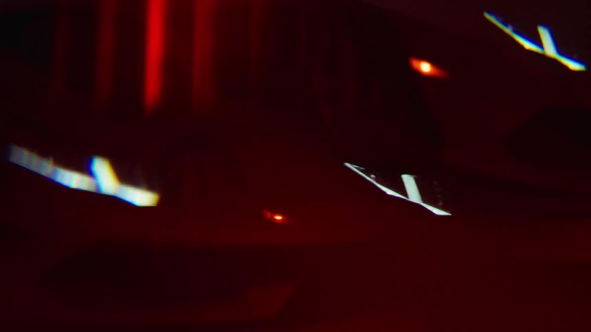 The front of a white lamborghini aventador illuminated by a saturated red light shifts in and out of focus