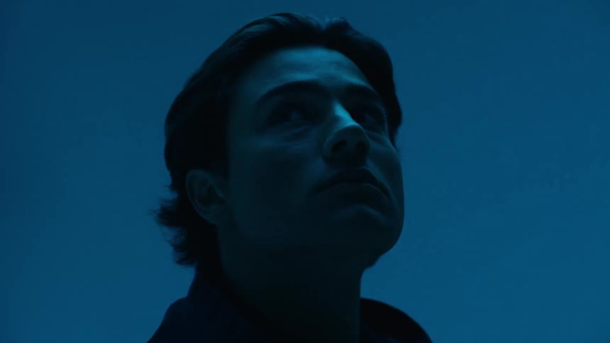 A man with dark hair looks upwards in a bluelit scene