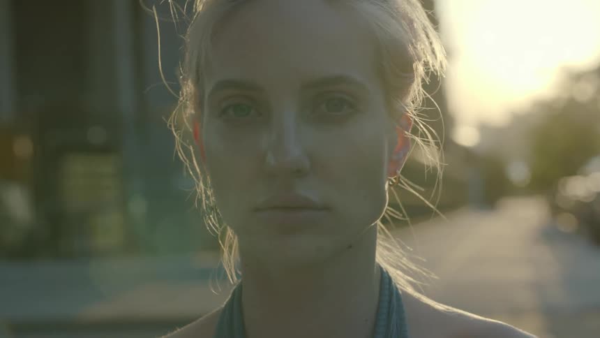 A woman stands on a city street with the sun shining behind her